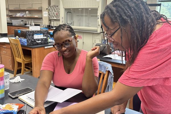Jessica Huff and Darfanda Mims-Scott working with D cell batteries, small lightbulb, and wires to create a complete circuit which will light the bulb.