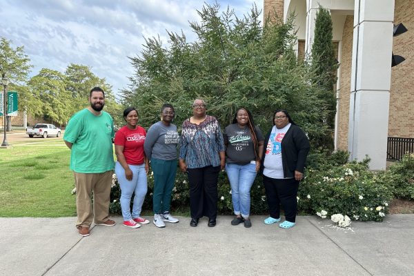 Five teachers posing for picture with Dr. Tayna McKinney in front of flowers and shrubbery.