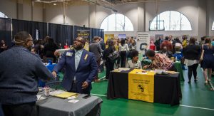 Students at career fair meeting with employers at tables.